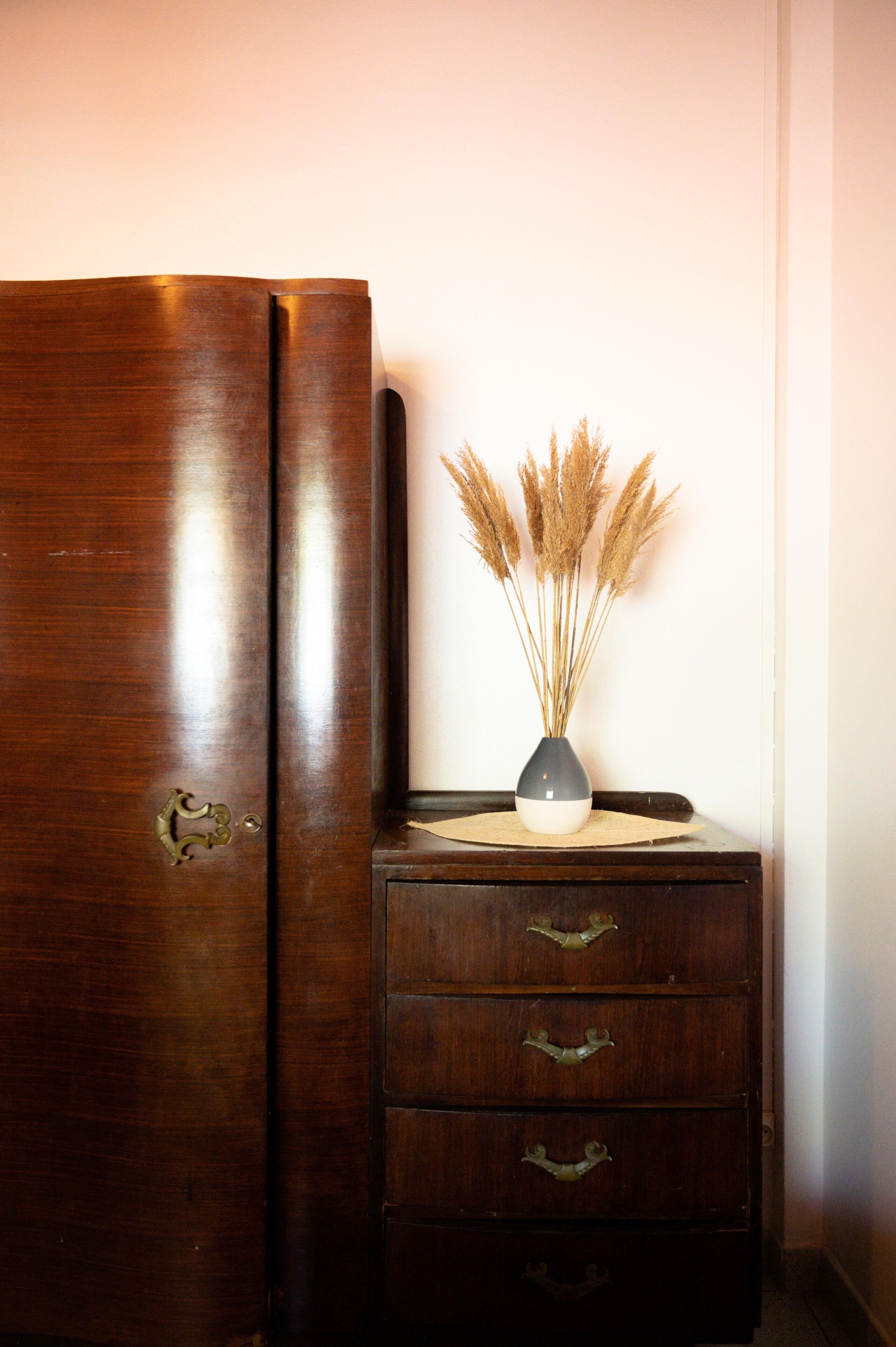 A wooden dresser with three drawers and a vase with dried plants on top.