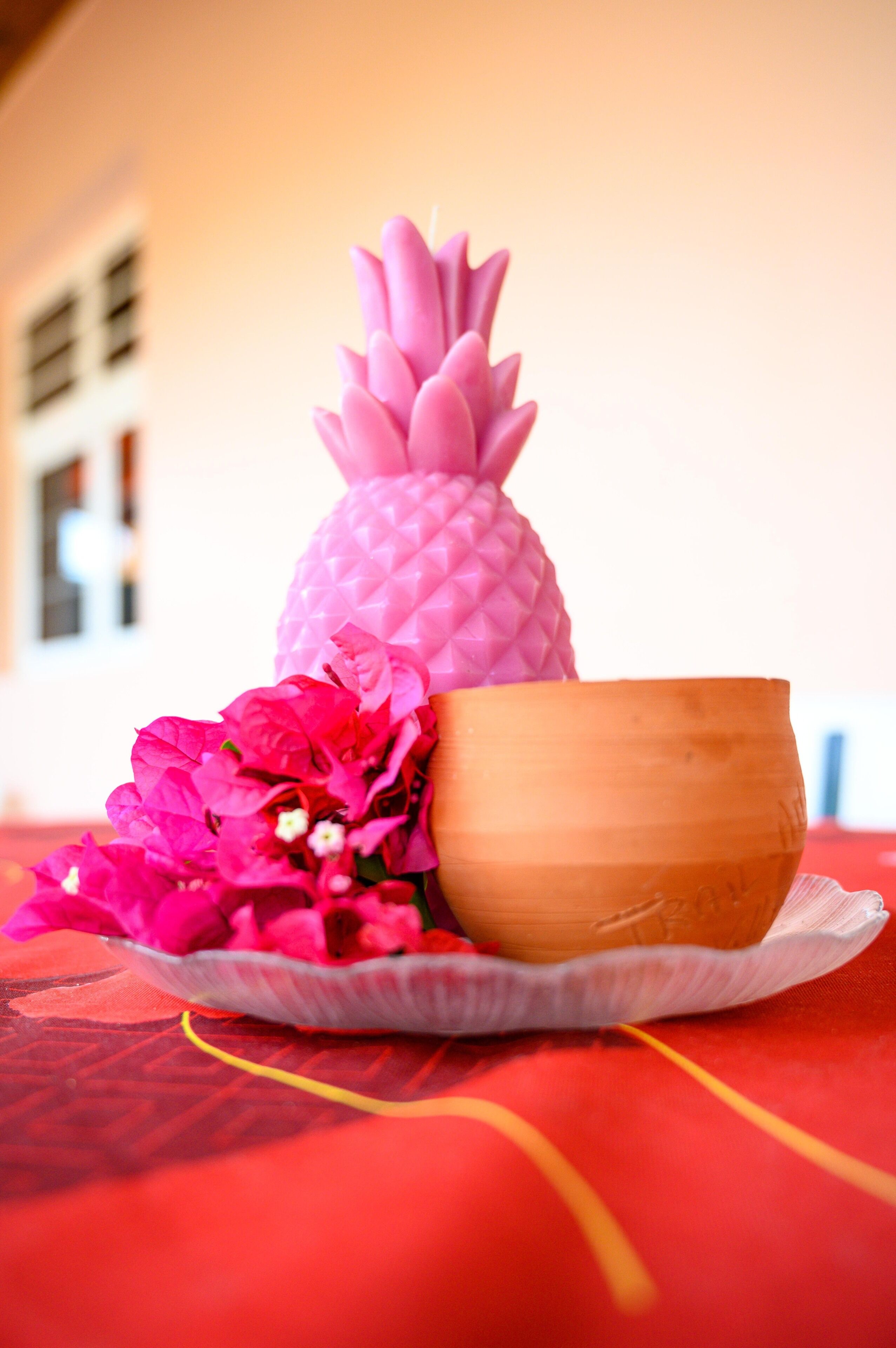 Uma decoração em formato de abacaxi, uma tigela e flores cor-de-rosa sobre uma toalha de mesa.