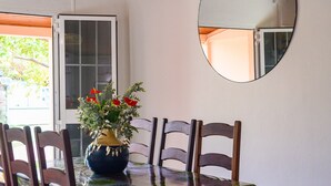 Un comedor con una mesa redonda, seis sillas de madera, un florero con flores y un espejo en la pared.
