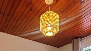 Un dormitorio con techo de madera, una cama con ropa de cama blanca y amarilla, una lámpara colgante y un tapiz en la pared.