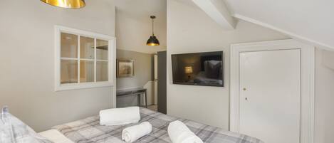 A bedroom with a bed, a window, a desk, a TV, and a door.