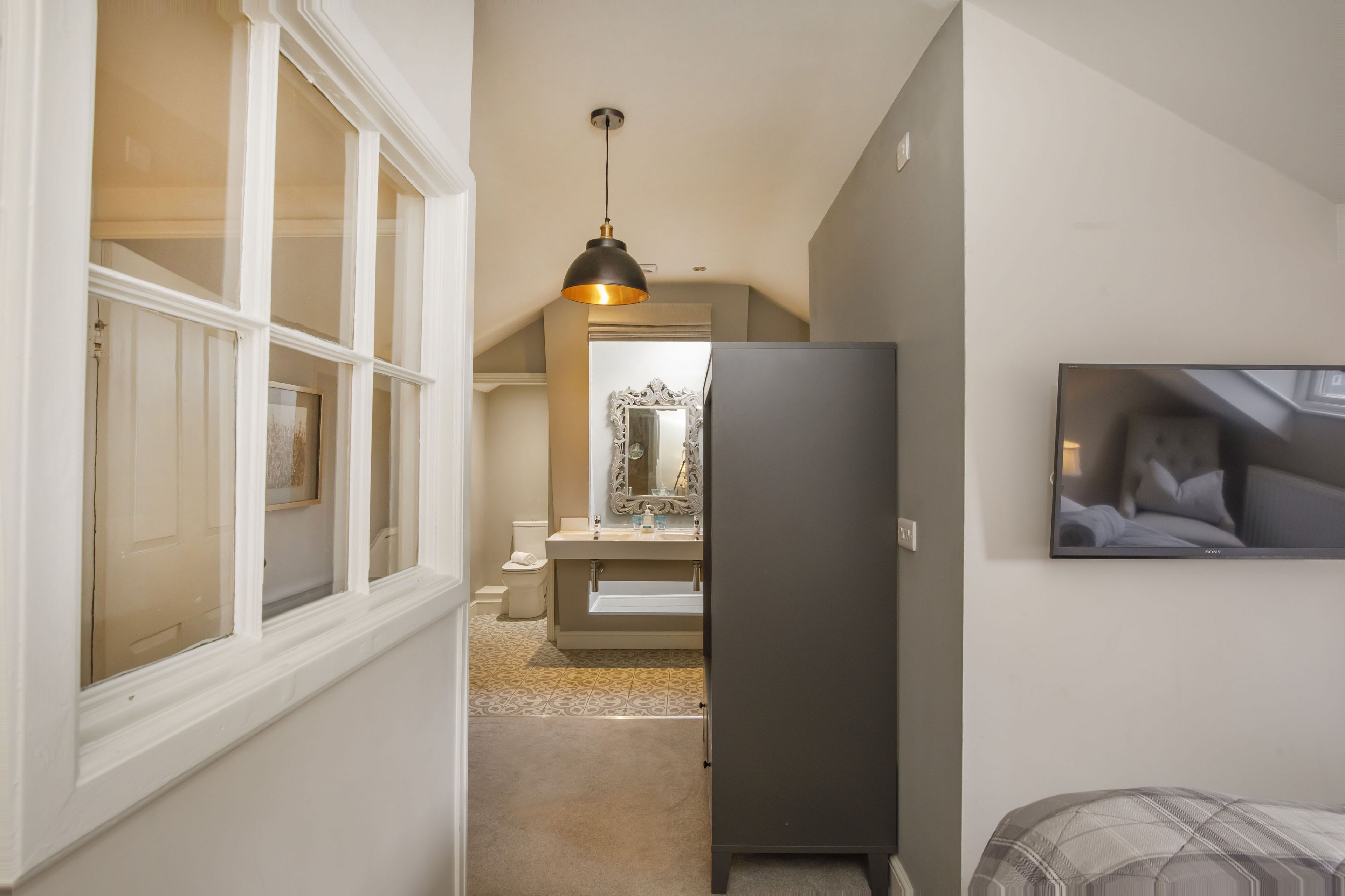 A narrow hallway with a window, a dark-colored refrigerator, a sink, and a bed with a plaid blanket.