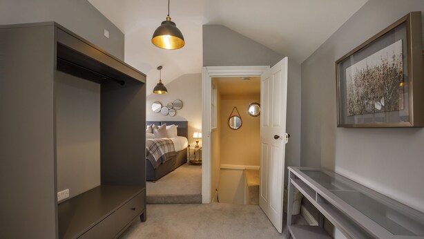 Een gang die leidt naar een slaapkamer met een bed, nachtkastje en een spiegel aan de muur.