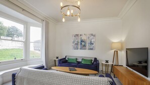 Een moderne woonkamer met een bank, salontafel en televisie. Twee schilderijen hangen aan de muur en een lamp staat op een bijzettafeltje.