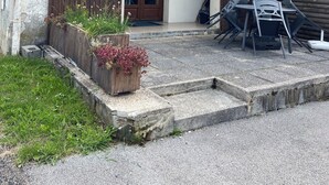 Um edifício de dois andares com fachada de madeira, varanda e uma pequena área externa com mesa e cadeiras.