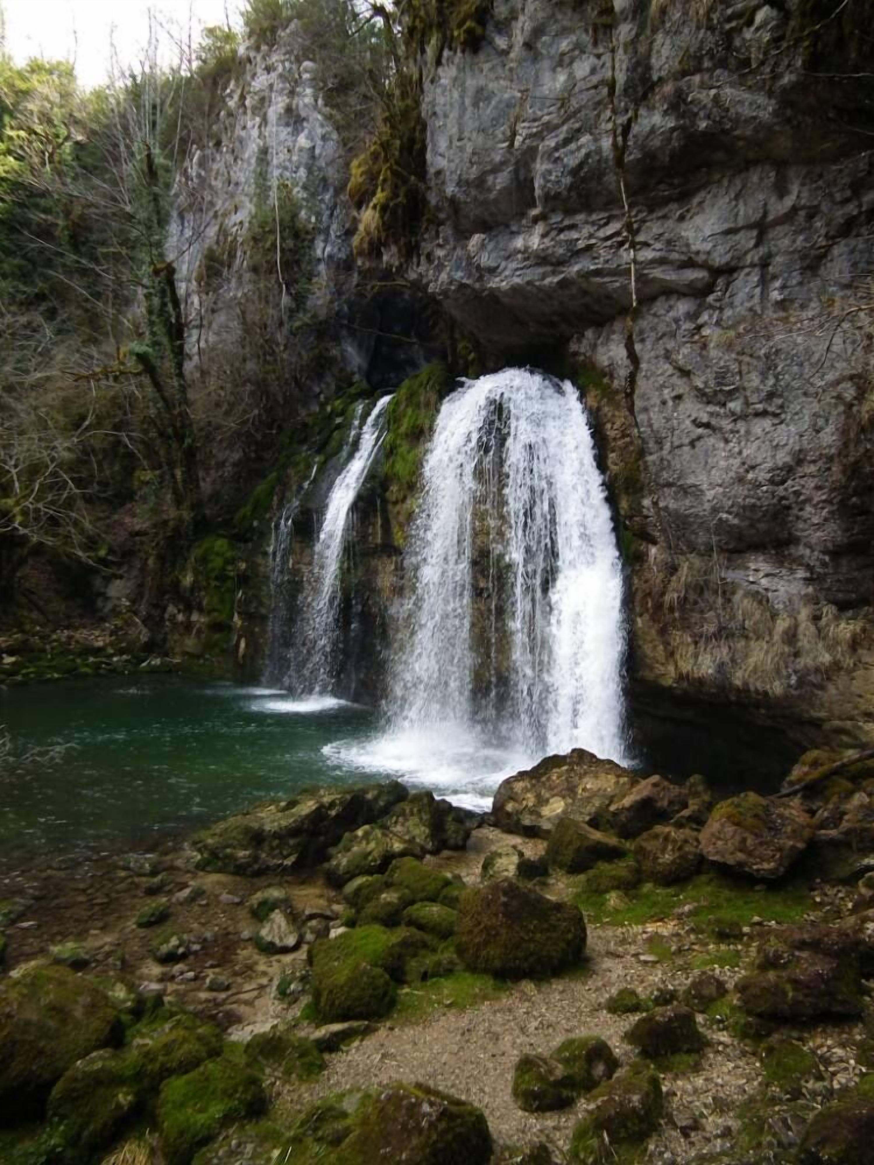 Ein natürlicher Wasserfall mit steiniger Vordergrundgestaltung und einem klaren Becken am Fuße.