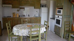 Cozinha com armários de madeira, mesa de jantar com cadeiras, geladeira e micro-ondas.