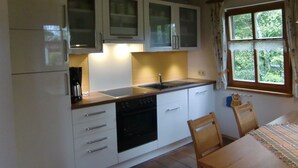 Una cocina compacta con armarios blancos, horno integrado y ventana con vista a zonas verdes.