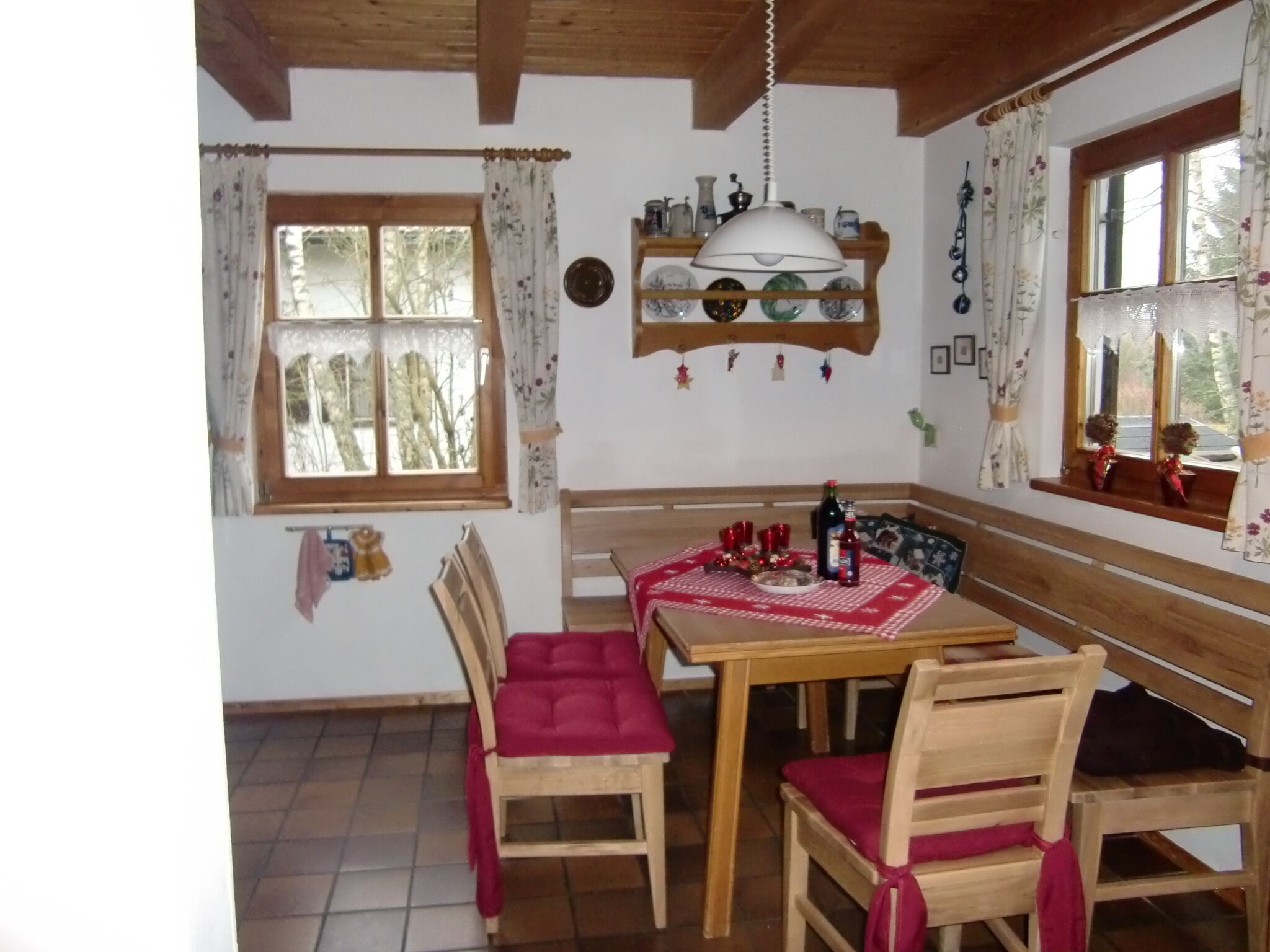 Un comedor con una mesa y sillas de madera, una lámpara colgante y una ventana con cortinas.