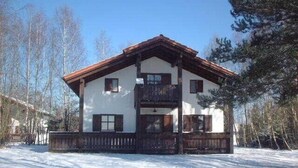 Una casa de madera de dos pisos con balcón, rodeada de nieve y árboles.