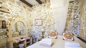 Ein Schlafzimmer mit Stehwänden, einem Bett, Handtüchern, einer Bank, einem Spiegel und einem kleinen Tisch mit einer Schale.