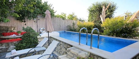 A backyard with a swimming pool, stone steps, lounge chairs, and a wooden fence.
