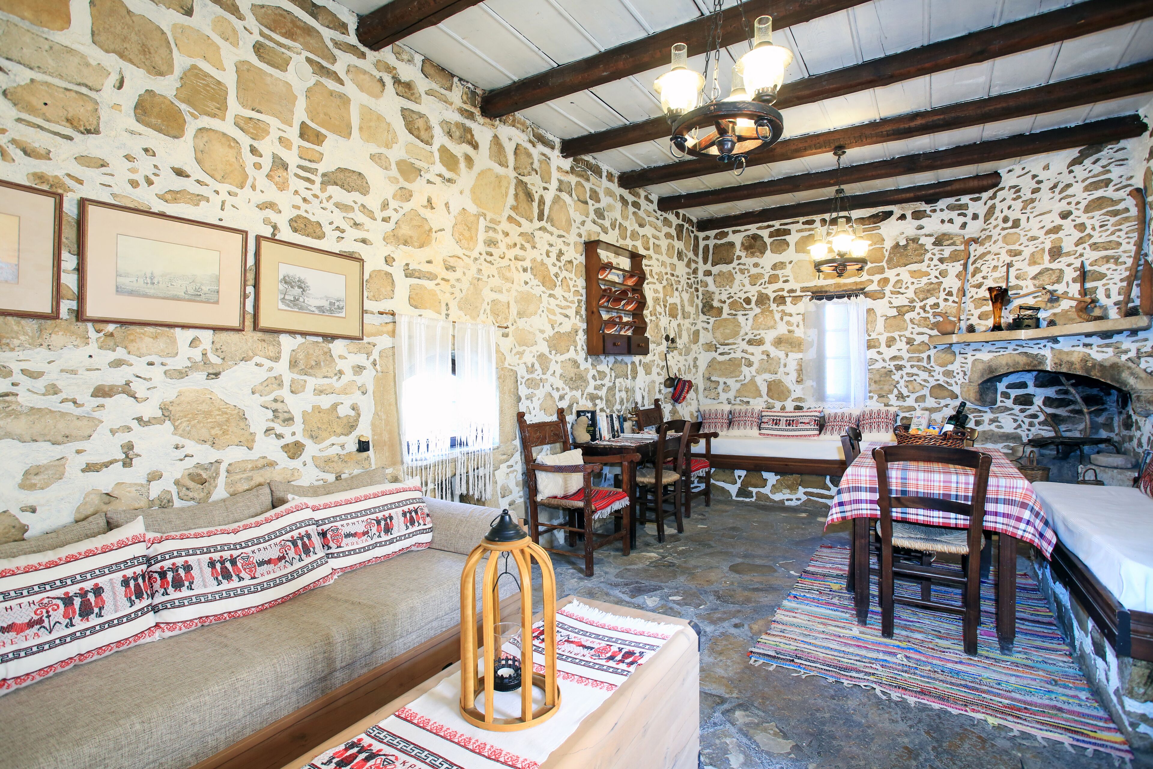 Una stanza rustica con pareti in pietra, soffitto in legno, un camino, un'area pranzo con tavolo e sedie e un divano con una coperta decorata.