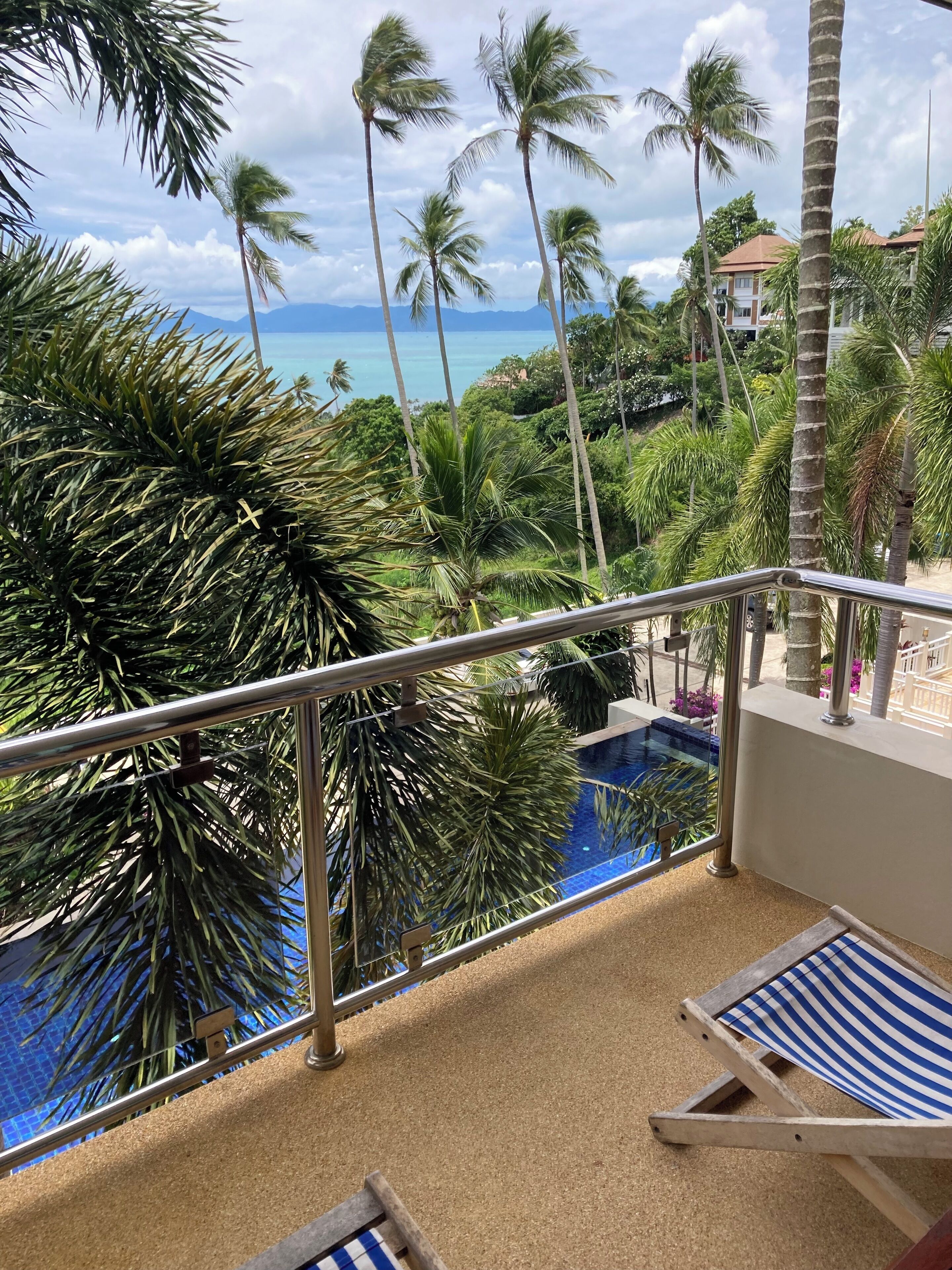 A balcony with a view of a pool and palm trees, overlooking a body of water and buildings.