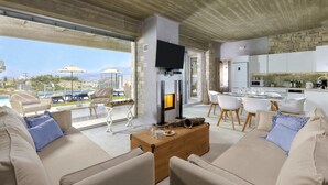 A modern living room with a fireplace, comfortable seating, and a view of the outdoors. - Kouros Villa (Faistos)