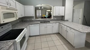 Una cocina con gabinetes blancos, microondas integrado, estufa y lavavajillas.