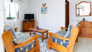 Un salon avec deux fauteuils en bois, une table basse en bois, un téléviseur posé sur un meuble en bois et un tableau encadré accroché au mur.