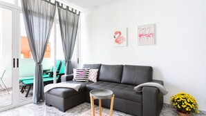 Een moderne woonkamer met een grijze bank, een klein rond tafeltje en een potplant.