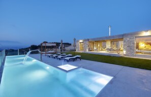 Un'area piscina moderna con lettini e un edificio in pietra con ampie finestre.