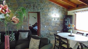 A cozy room with a stone wall, a wooden ceiling, a dining table with chairs, and a sofa with cushions.