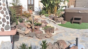 A garden with a stone pathway, various plants, a wooden bench, and a small wooden structure.