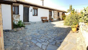 A stone-paved courtyard with a rustic building featuring a wooden bench and potted plants.