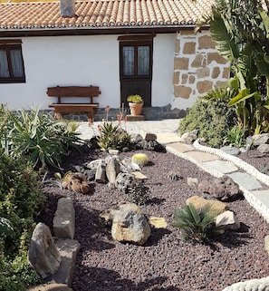 A stone house with a tiled roof, a wooden bench, and a garden with rocks and plants. - Romantic country house, with Whirlpool (Villa de Arico)