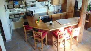 A compact kitchen with wooden cabinets, a central island with stools, a sink, and various kitchen appliances.