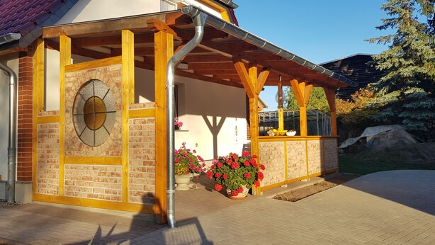 A covered outdoor area with a brick wall, wooden beams, and a metal door with a window.
