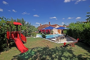 Un patio trasero con un tobogán rojo, una piscina y un porche cubierto.