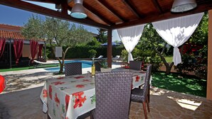 An outdoor patio with a pool, covered seating area, and a table set for dining.