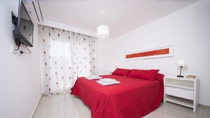 Een keurig opgemaakt slaapkamer met een bed, een nachtkastje, een lamp en een aan de muur bevestigde televisie.
