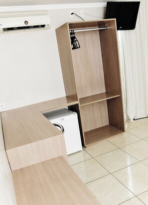 A modern room with a built-in air conditioning unit, a flat-screen TV mounted on the wall, and a wooden cabinet with a built-in refrigerator. - Vivendas Hotel (Erechim)