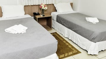 A hotel room with two beds, a nightstand, a vase with flowers, and a rug.