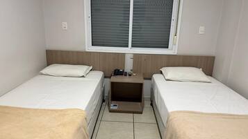 Una habitación con dos camas, una mesita de noche pequeña con un teléfono y una ventana con persianas.