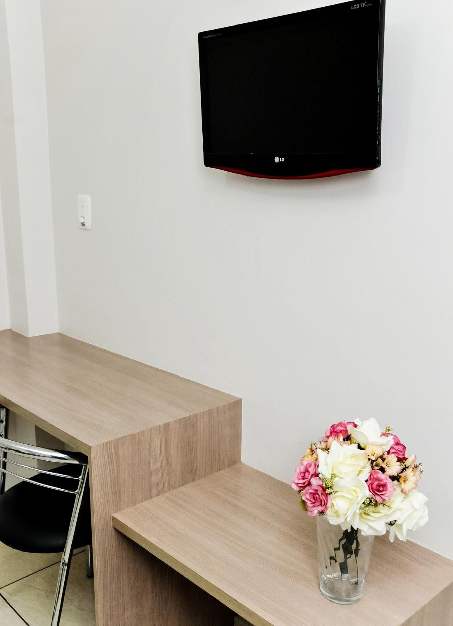 Habitació moderna amb televisió de pantalla plana penjada a la paret, escriptori de fusta, una cadira i un ram de flors.