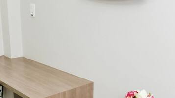 Habitació moderna amb televisió de pantalla plana penjada a la paret, escriptori de fusta, una cadira i un ram de flors.