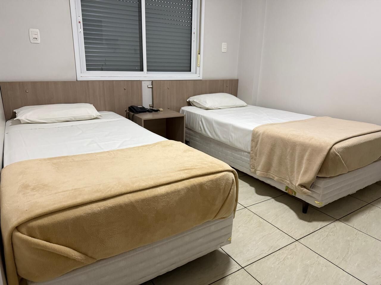 Habitación de hotel con dos camas, una mesita de noche y una ventana con persianas.