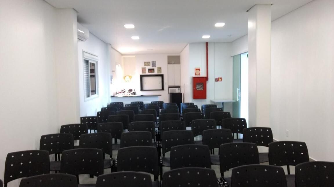 A conference room with rows of black chairs, white walls, and a kitchenette area in the background.