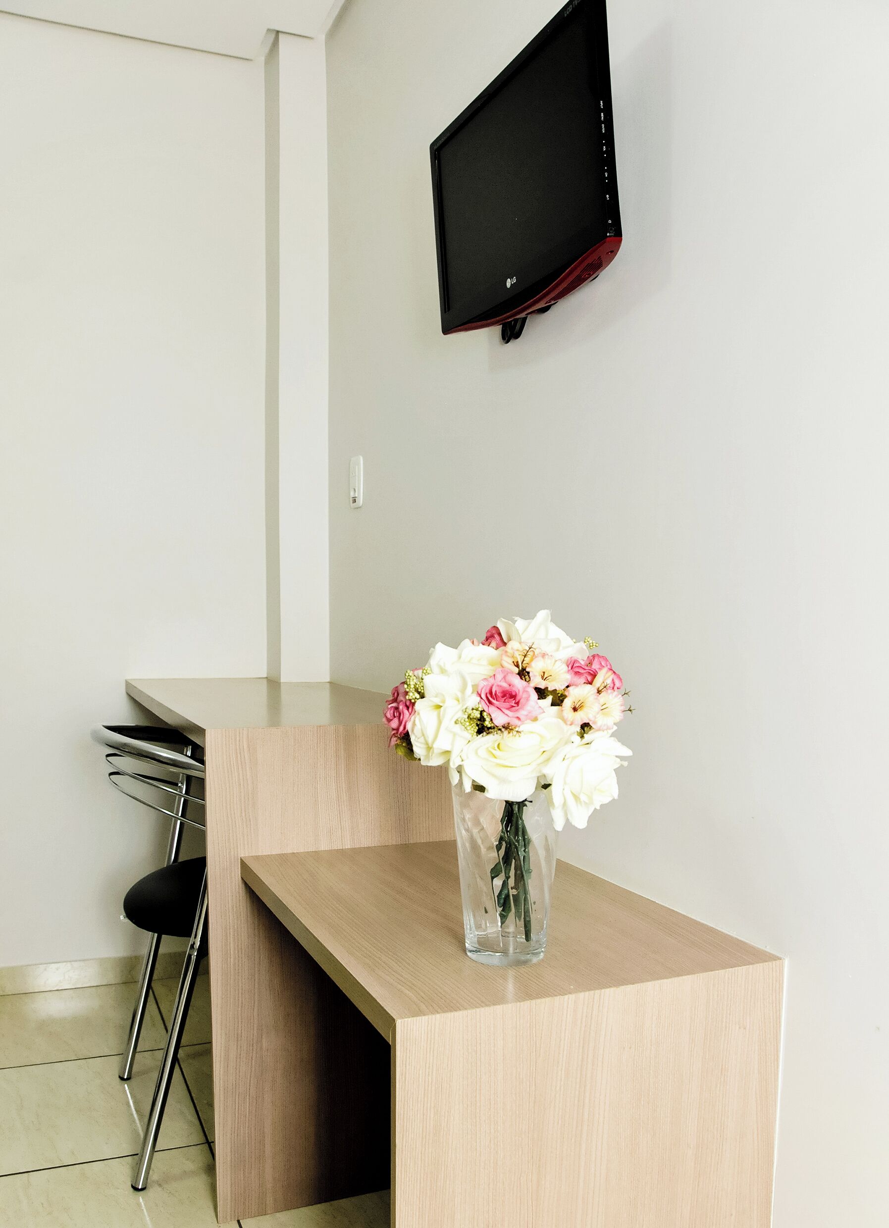 Un mostrador de recepción con un jarrón de flores, un televisor de pantalla plana y una silla.