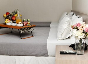 Una sala de estar moderna con un sofá gris, una mesita con aperitivos y bebidas, un jarrón con flores y un control remoto sobre una mesita de madera.
