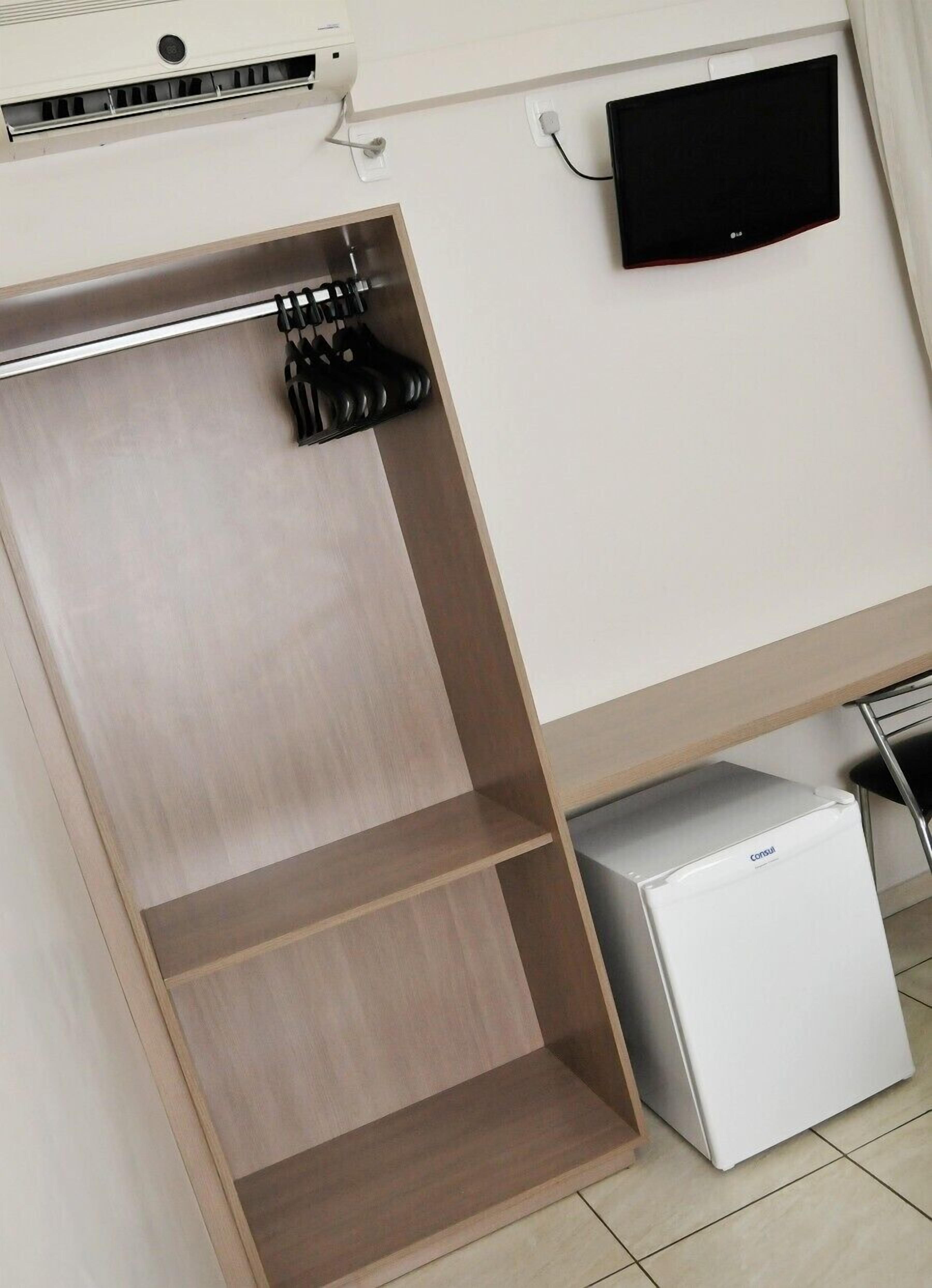 A wardrobe with a mirror, a flat-screen TV mounted on the wall, and a small white appliance on the floor.