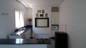 A kitchen with a stove, microwave, and cabinets. There are framed pictures on the wall. - Vivendas Hotel (Erechim)
