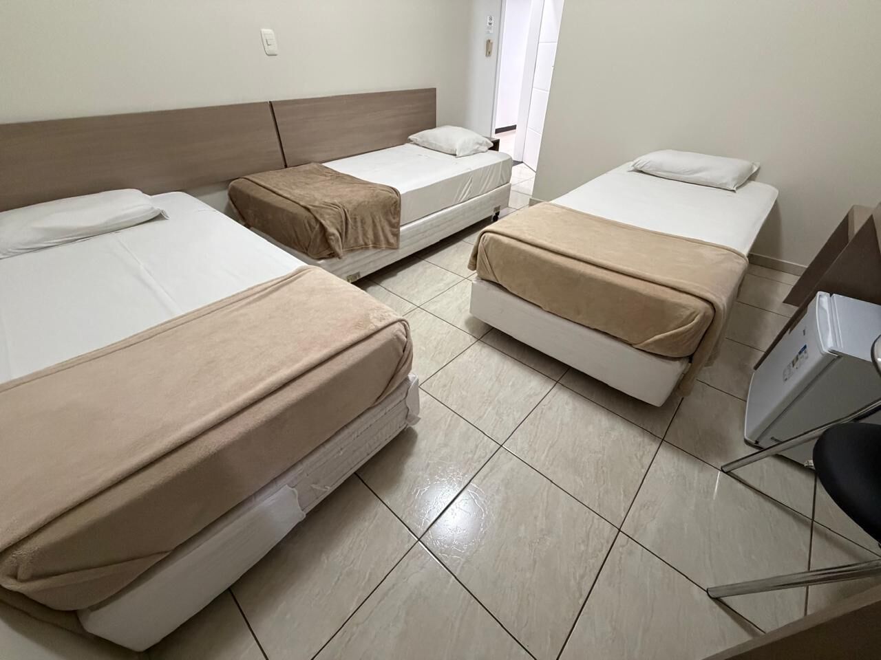 Una camera d'albergo con tre letti, una scrivania e una sedia.