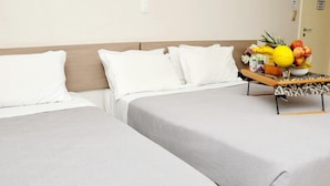 A hotel room with two beds, white bedding, a wooden headboard, and a fruit bowl on a side table. - Vivendas Hotel (Erechim)
