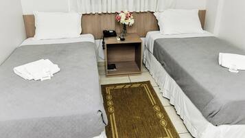 Habitación de hotel con dos camas, una mesita de noche con teléfono, un florero con flores y una alfombra marrón.