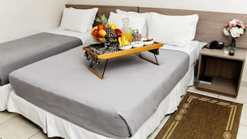 Quarto de hotel com duas camas, uma mesinha de cabeceira com telefone, um vaso com flores e uma bandeja com frutas e uma garrafa.