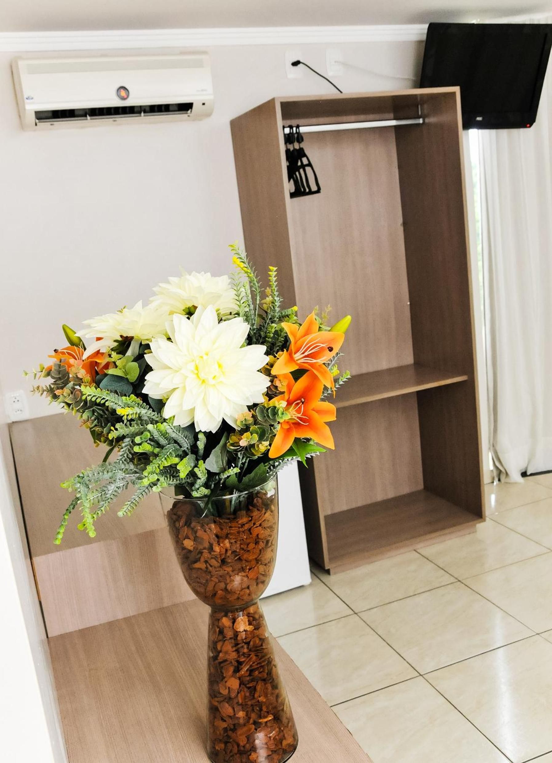A room with a wooden cabinet, a white air conditioning unit, and a clear glass vase with flowers on a wooden table.