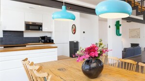 Una cocina moderna con armarios blancos, una mesa de comedor de madera y lámparas colgantes azules.