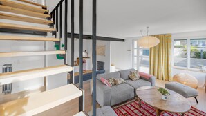 Una sala de estar moderna con un sofá gris, una mesa redonda de centro y una escalera con escalones de madera.
